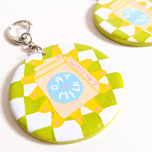 Load image into Gallery viewer, Keyring with round clay pendant painted with green and white checkered background and oat milk drawing